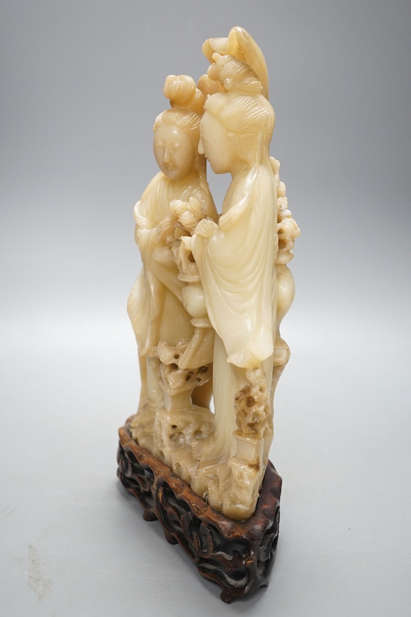 A Chinese soapstone carving of two ladies, wood stand, early 20th century, 36 cms high.